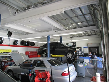 Galceran Auto Electric garage with mechanics working. There is one car on a lift and one car with the hood open. Tires are visible in the background on a shelf